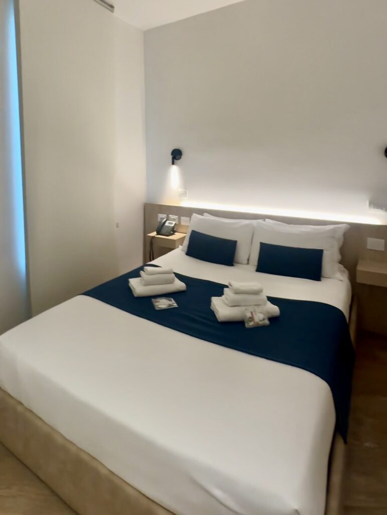 Double bed with white bedding, a navy runner and folded towels in my HelloSky room.
